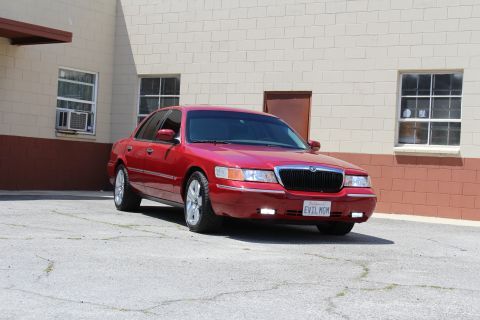 2002 Mercury Grand Marquis - A red 2002 Mercury Grand Marquis is parked outside a building with a license plate that reads EVIL MGM.