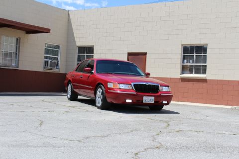 2002 Mercury Grand Marquis - A red 2002 Mercury Grand Marquis is parked in a lot with a brick building in the background.