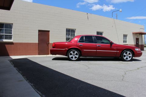 2002 Mercury Grand Marquis - A red 2002 Mercury Grand Marquis is parked in front of a commercial building on a sunny day.
