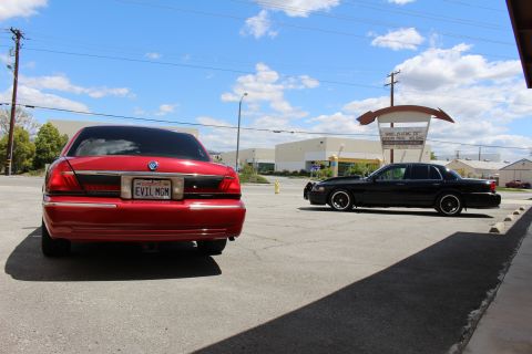 2002 Mercury Grand Marquis - Two sedans are parked in a lot on a sunny day. The red sedan is in the foreground.