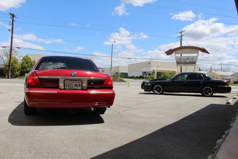 2002 Mercury Grand Marquis - A red Mercury Grand Marquis is parked in a lot next to a black car under a cloudy sky.