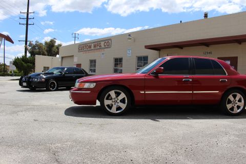 2002 Mercury Grand Marquis - A red 2002 Mercury Grand Marquis is parked next to a black sedan in front of a building.