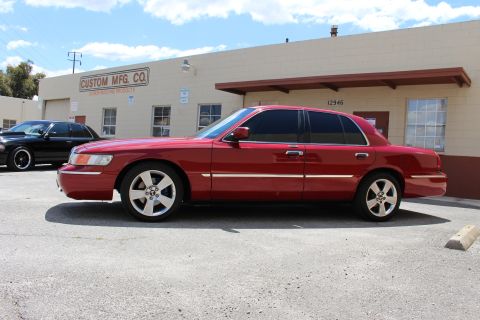 2002 Mercury Grand Marquis - A red sedan is parked in front of a commercial building, with another car visible behind it.