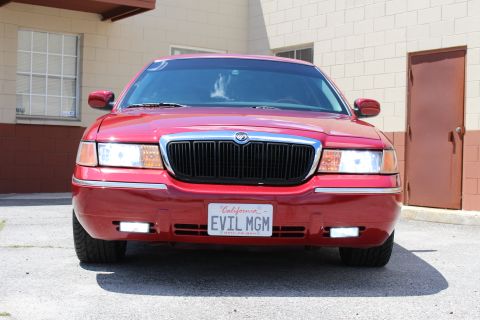 2002 Mercury Grand Marquis - A red 2002 Mercury Grand Marquis is parked in front of a brick building with a brown door.