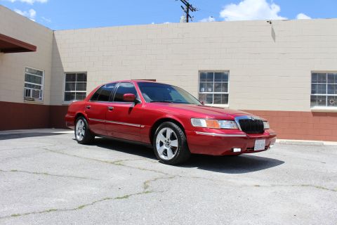 2002 Mercury Grand Marquis - A red 2002 Mercury Grand Marquis is parked in an outdoor lot next to a brick building.