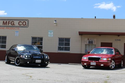 2002 Mercury Grand Marquis - Two sedans, a red 2002 Mercury Grand Marquis and a black modified sedan, are parked in front of a commercial building.