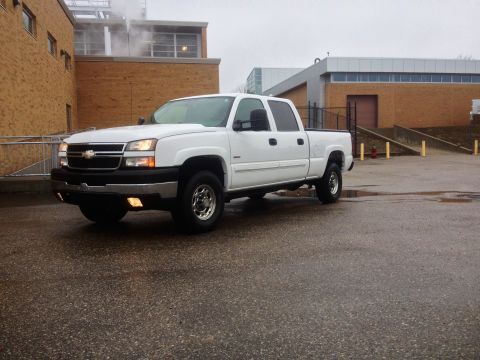2006 Chevrolet Silverado 2500 - A white 2006 Chevrolet Silverado 2500 pickup truck is parked on a wet asphalt surface in front of a brick building.