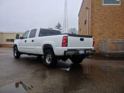 2006 Chevrolet Silverado 2500 - White pickup truck parked on wet asphalt with a brick building in the background.