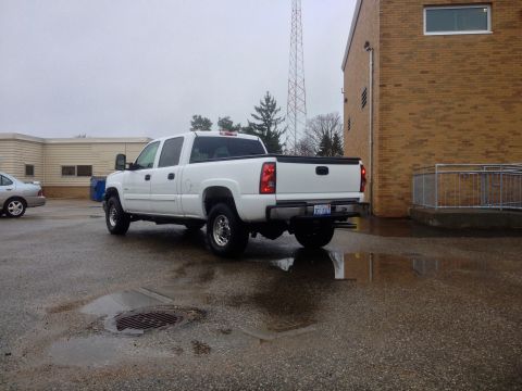 2006 Chevrolet Silverado 2500 - A white 2006 Chevrolet Silverado 2500 pickup truck is parked in a wet lot, viewed from the rear 3/4 angle.