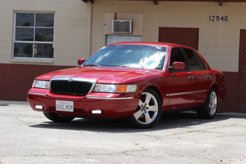 2002 Mercury Grand Marquis - A red 2002 Mercury Grand Marquis is parked in front of a brick building with an air conditioning unit visible.
