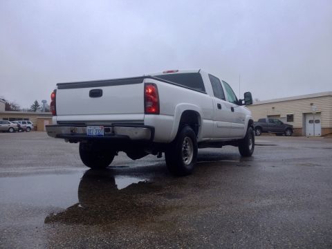 2006 Chevrolet Silverado 2500 - A white 2006 Chevrolet Silverado 2500 pickup truck is parked on wet asphalt under an overcast sky.