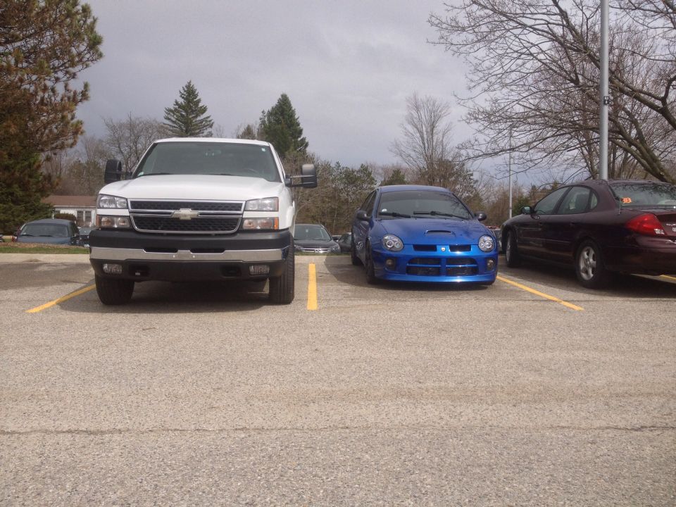 White pickup truck parked next to a blue Dodge Neon SRT-4. Another car is parked to the right