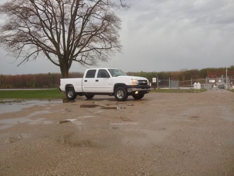 2006 Chevrolet Silverado 2500 - A white pickup truck is parked on wet ground with a large tree in the background.