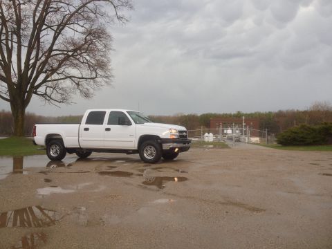 2006 Chevrolet Silverado 2500 - A white 2006 Chevrolet Silverado 2500 crew cab pickup truck is parked outside on a cloudy day with puddles on the ground.