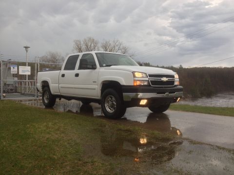 2006 Chevrolet Silverado 2500 - A white 2006 Chevrolet Silverado 2500 pickup truck is parked on a grassy area next to a fence and a body of water under a cloudy sky.