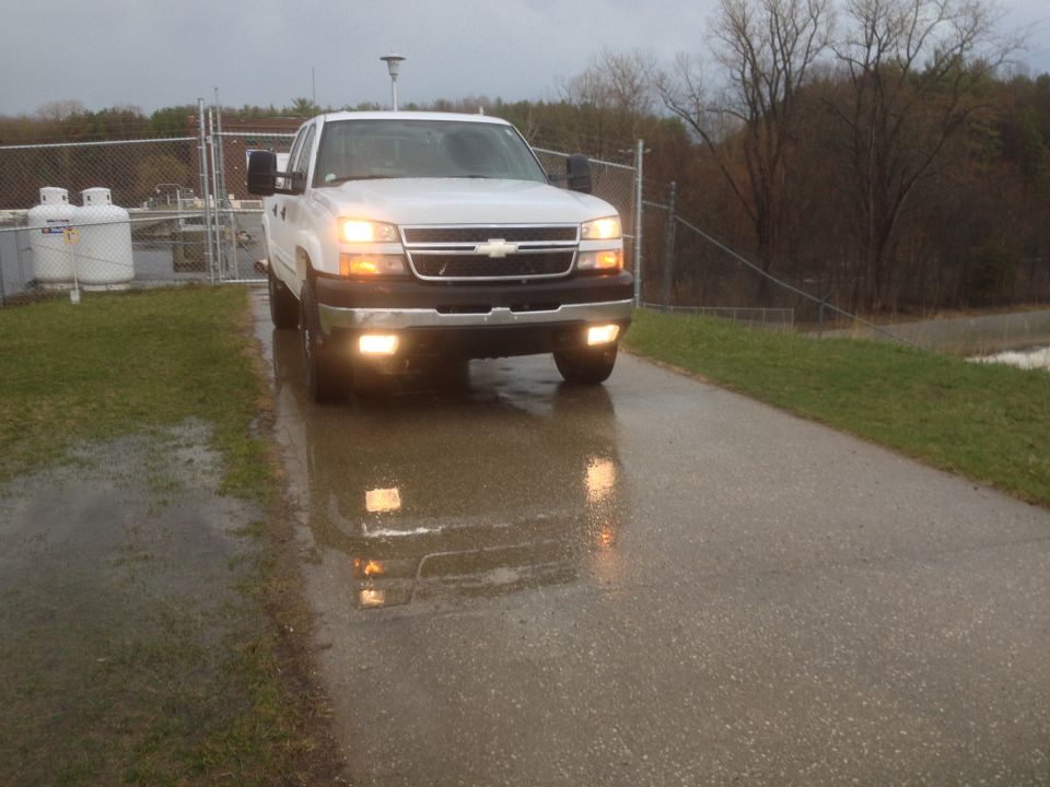 White pickup truck with headlights on, parked on a wet road