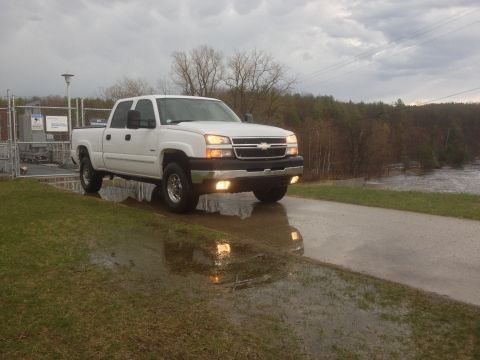 2006 Chevrolet Silverado 2500 - A white pickup truck is parked on a wet road next to a body of water under a cloudy sky.