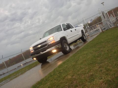 2006 Chevrolet Silverado 2500 - A white pickup truck is angled on a wet road with grass on the side under a cloudy sky.