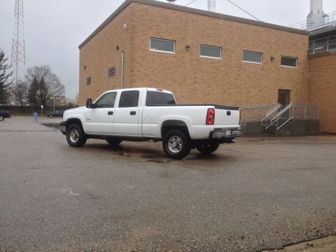 2006 Chevrolet Silverado 2500 - A white Chevrolet Silverado pickup truck is parked in a lot next to a brick building on an overcast day.