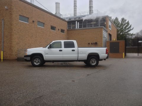 2006 Chevrolet Silverado 2500 - A white pickup truck is parked on a wet asphalt surface outside a brick industrial building.