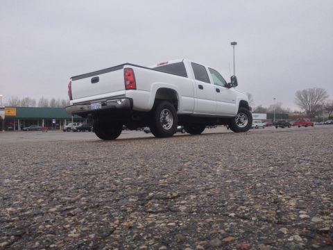 2006 Chevrolet Silverado 2500 - A white pickup truck is parked in a lot with other vehicles and buildings in the background.