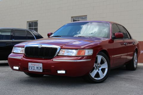 2002 Mercury Grand Marquis - A red 2002 Mercury Grand Marquis is parked in front of a building, with another car behind it.