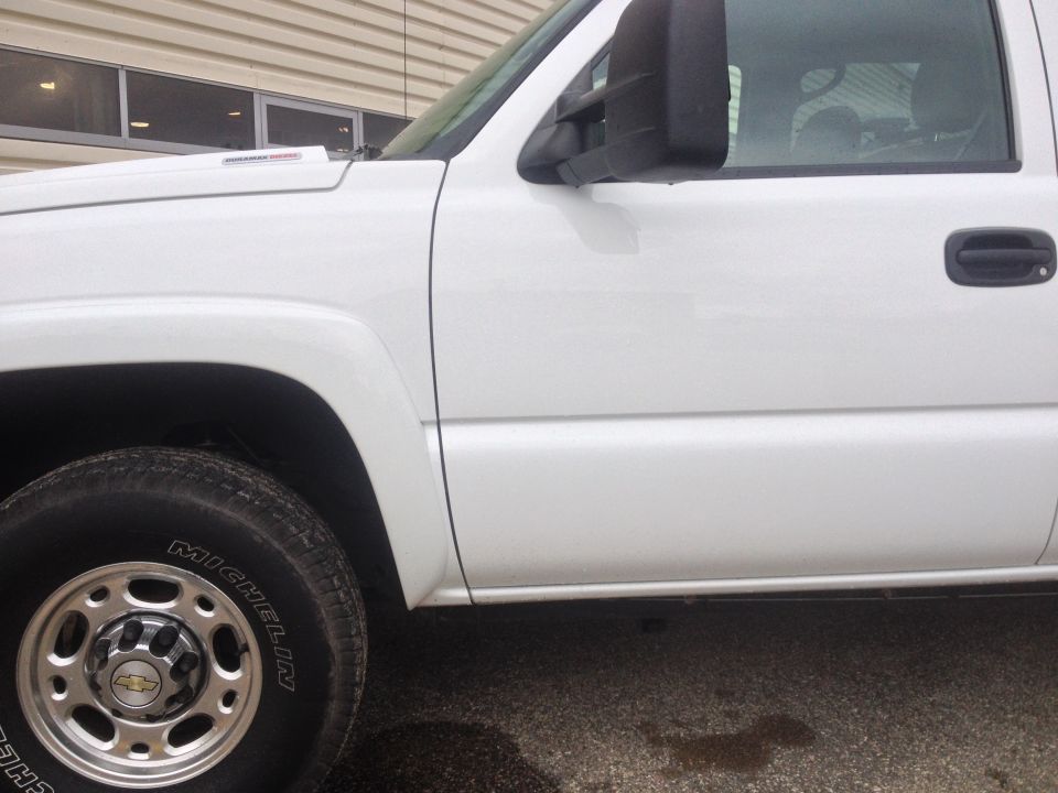 Side view of a white Chevrolet Silverado pickup truck, showing the front fender, door, and wheel