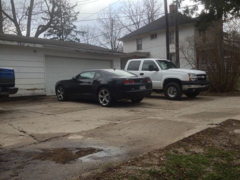 2006 Chevrolet Silverado 2500 - A black coupe and a white pickup truck are parked in front of a garage and house.