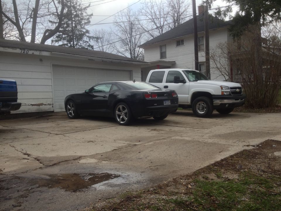 Black coupe parked next to a white pickup truck in a driveway
