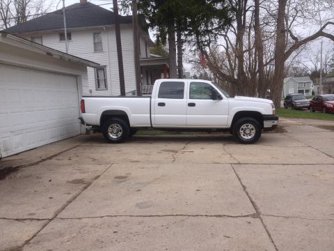 2006 Chevrolet Silverado 2500 - A white crew cab pickup truck is parked on a concrete driveway next to a white garage.
