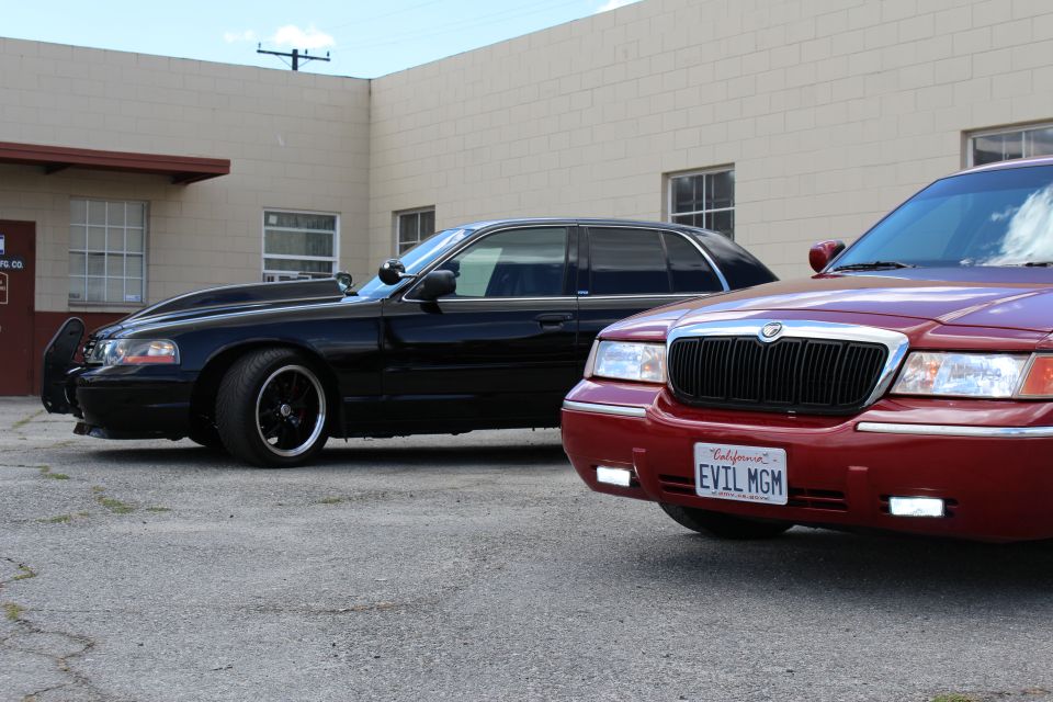 Red Mercury Grand Marquis with custom grille and black hood, parked next to a black Mercury Grand Marquis with a modified hood