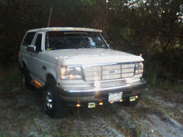 White Ford Bronco with aftermarket lights on the front bumper and roof visor