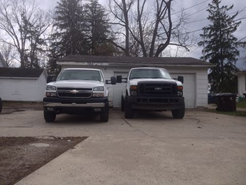 2006 Chevrolet Silverado 2500 - Two trucks are parked in front of a garage. The truck on the left appears to be a Chevrolet Silverado, while the truck on the right is a Fo…
