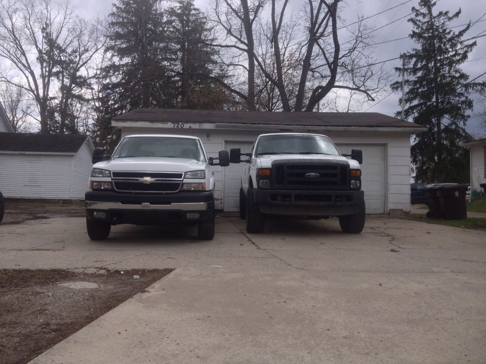 Two pickup trucks parked in front of a garage. One is a Chevrolet Silverado, the other is a Ford