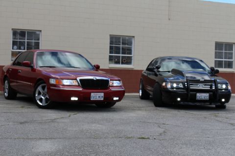 2002 Mercury Grand Marquis - Two sedans, a red Mercury Grand Marquis and a black Ford Crown Victoria, are parked outside a building.