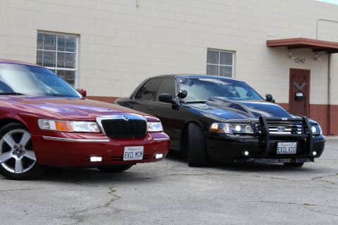 2002 Mercury Grand Marquis - Two Mercury Grand Marquis sedans are parked in front of a building, one red and one black with custom modifications.