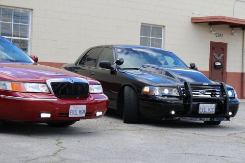 2002 Mercury Grand Marquis - Two sedans, one red Mercury Grand Marquis and a black modified sedan, are parked side-by-side.