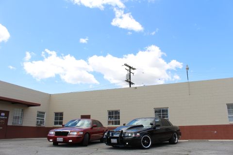 2002 Mercury Grand Marquis - Two sedans, one red and one black, are parked in front of a building on a sunny day.