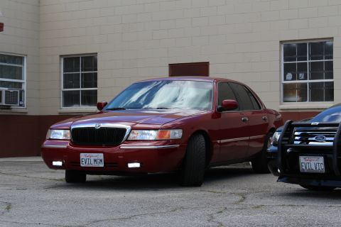 2002 Mercury Grand Marquis - A red 2002 Mercury Grand Marquis sedan is parked next to another vehicle, with the license plate 'EVIL MGM' visible.