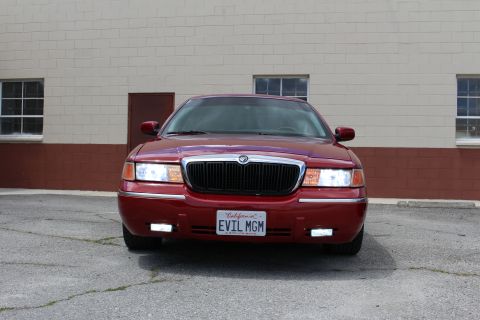 2002 Mercury Grand Marquis - Front view of a red 2002 Mercury Grand Marquis parked in front of a brick building.