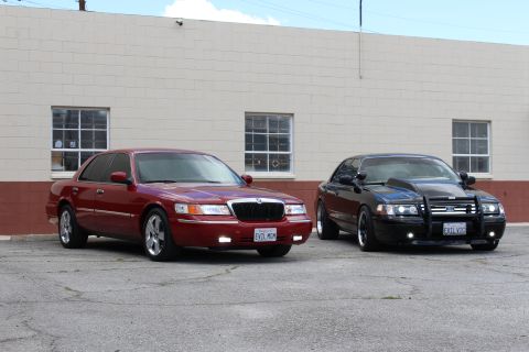 2002 Mercury Grand Marquis - Two sedans, a red Mercury Grand Marquis and a black modified sedan, are parked outside a building.