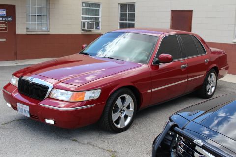 2002 Mercury Grand Marquis - A red 2002 Mercury Grand Marquis is parked outside a building, with another vehicle partially visible in the foreground.