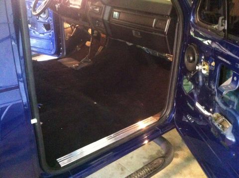 1982 Ford Bronco - The interior of a blue vehicle shows new black carpeting and exposed door mechanisms.