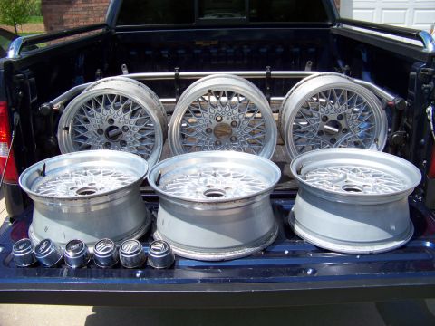 1999 Mercury Grand Marquis - Six bare aluminum lace/mesh-spoke alloy wheels stood up in the bed of a dark blue pickup, three showing their faces and three showing barre…
