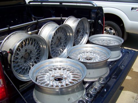 1999 Mercury Grand Marquis - A collection of aftermarket mesh wheels are stored in the bed of a dark-colored pickup truck, with another truck visible behind.