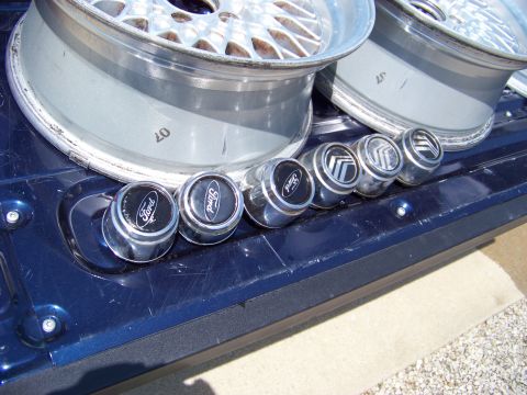 1999 Mercury Grand Marquis - Wheel center caps and rims are displayed on a dark blue surface, with visible Ford and Mercury branding.