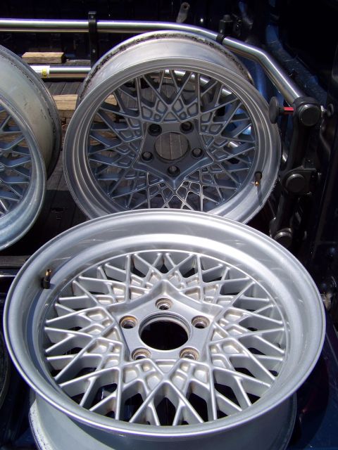 1999 Mercury Grand Marquis - A set of silver wire wheels with a distinctive starburst spoke pattern is displayed, likely for sale or transport.