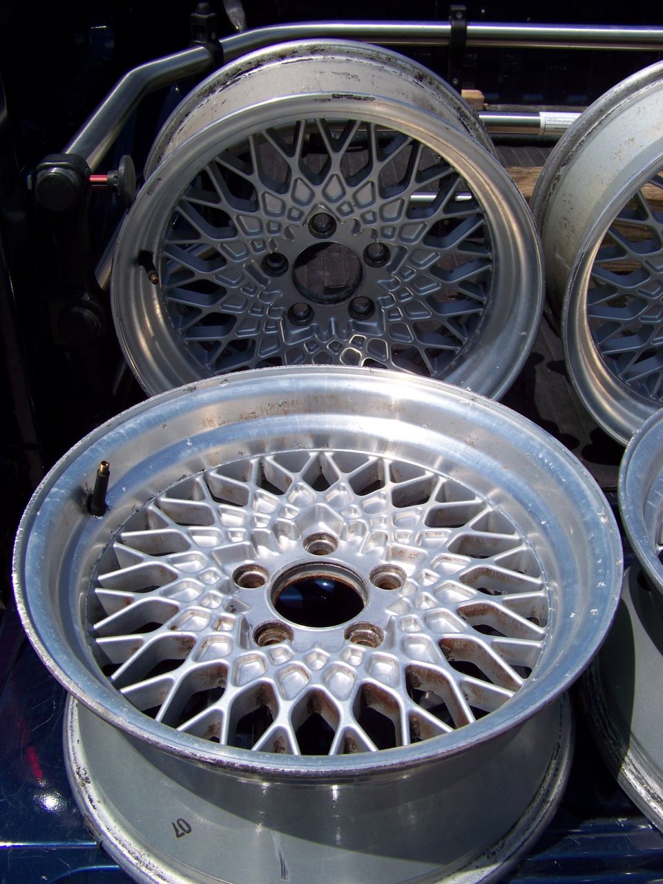 Four mesh alloy wheels stacked in a truck bed