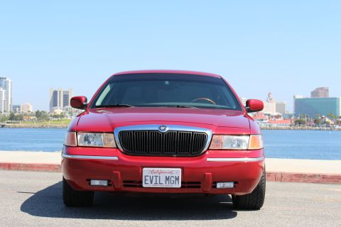 2002 Mercury Grand Marquis - A red Mercury Grand Marquis is parked by the water with a city skyline in the background.