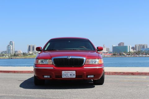 2002 Mercury Grand Marquis - A red 2002 Mercury Grand Marquis is seen from the front with a city skyline in the background.